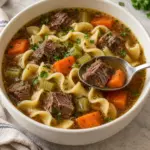 Overhead view of beef noodle soup with chuck, egg noodles, carrots, celery and parsley.