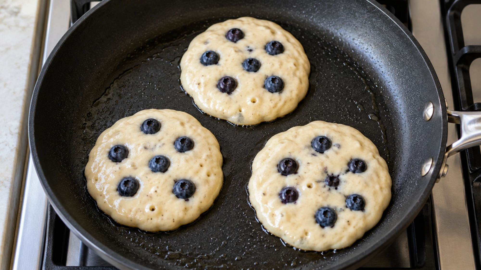 Three blueberry tofu pancakes cooking in a skillet before their first flip.