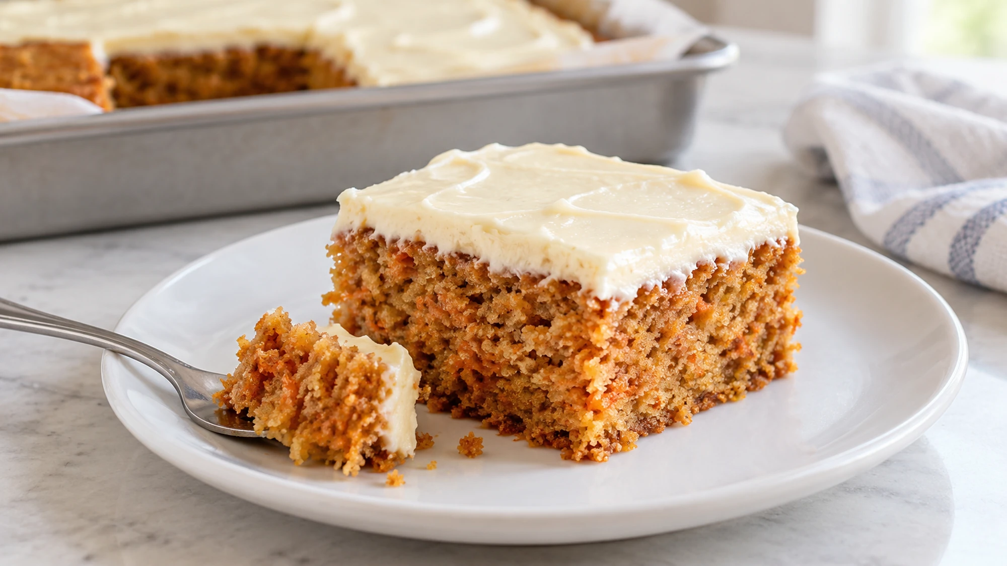 Carrot cake square with cream cheese frosting and fine carrot flecks in the crumb.