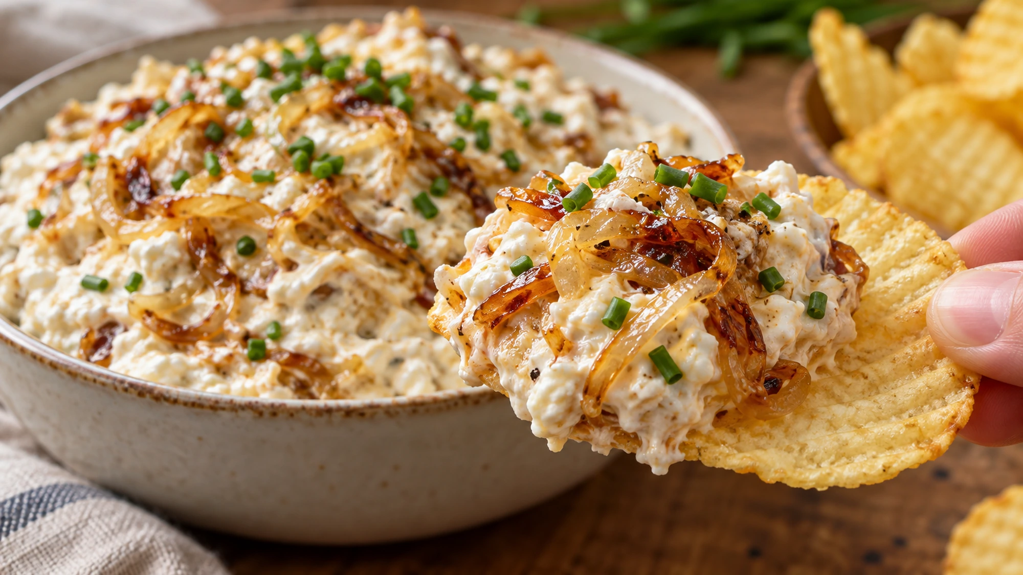Potato chip lifting cottage cheese caramelized onion dip from a bowl