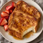 Square view of golden French toast with a soft cooked center and optional strawberry topping