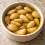 Square recipe image of garlic confit cloves fully submerged in olive oil