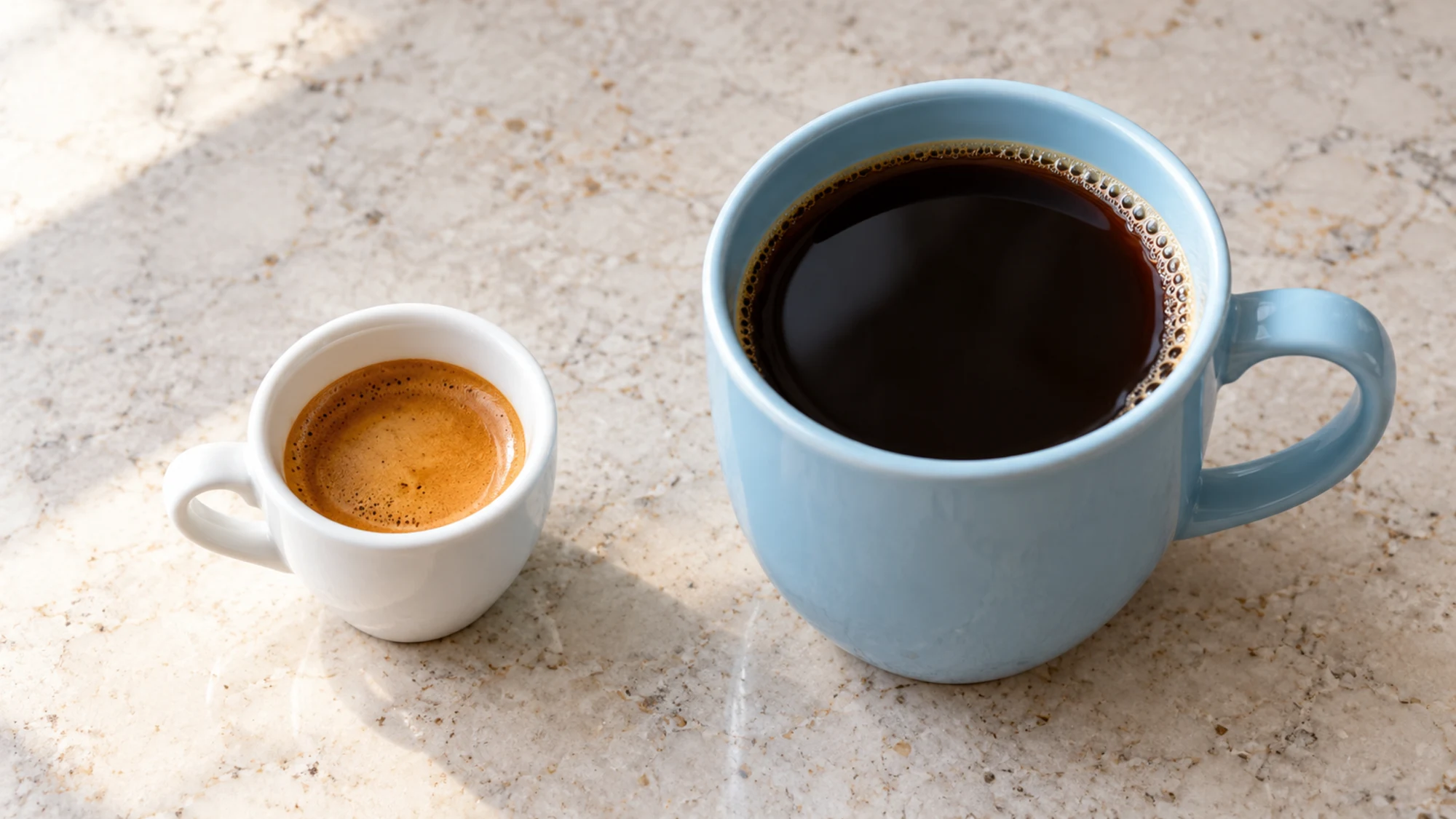 A small espresso cup beside a larger mug of black coffee.