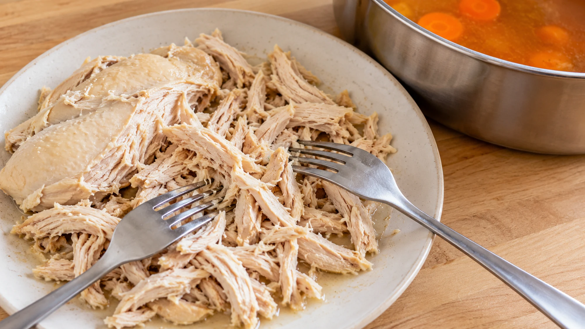 Cooked chicken breast being shredded with two forks for caldo tlalpeño.